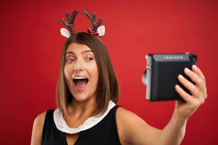 Adult happy woman in Christmas mood taking instant pictures over red background
