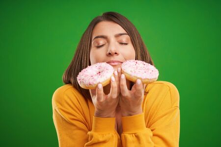 Beautiful woman posing with donuts over green backgroundの写真素材