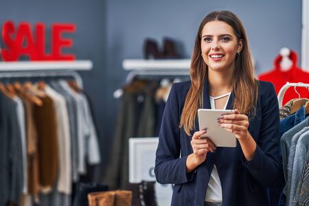 Happy shop assistant in her boutique with winter autumn collectionの写真素材