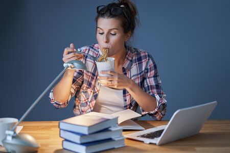 Hungry student eating noodle while learning at home