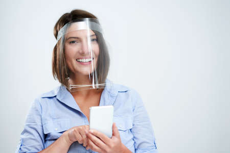 Woman wearing protective mask holding smartphone over white backgroundの写真素材