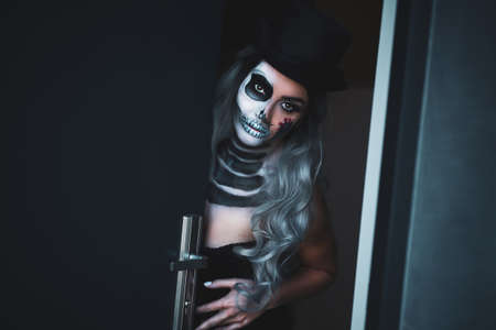 Spooky portrait of woman in halloween gotic makeup opening doorの写真素材