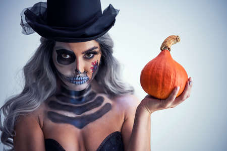 Spooky portrait of woman in halloween gotic makeup holding pumpkin
