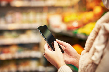 Adult woman in medical mask using smartphone and shopping for groceriesの写真素材