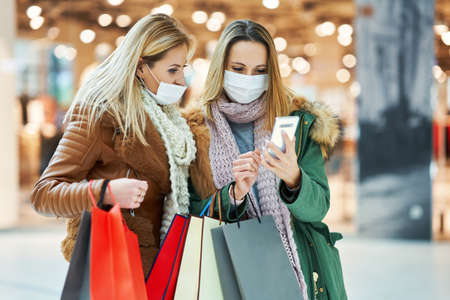 Girl friends with smartphone shopping together wearing mask coronavirus conceptの写真素材