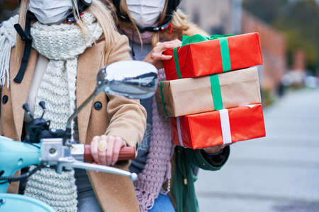 Two women wearing masks and holding shopping bags on scooterの写真素材
