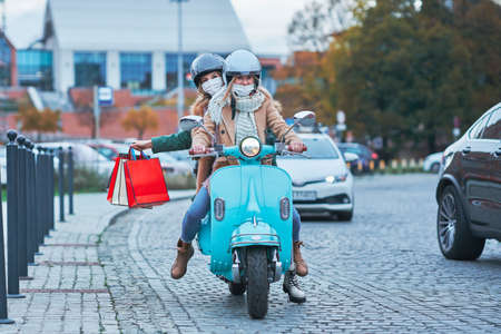 Two women wearing masks and holding shopping bags on scooterの写真素材
