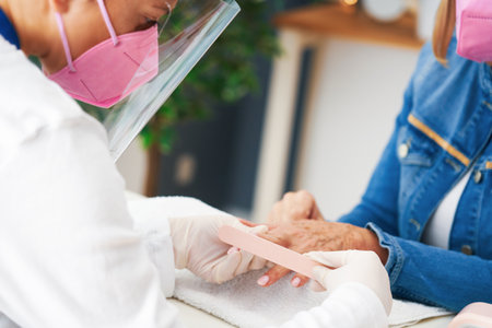 Senior lady wearing a mask in manicure salonの写真素材