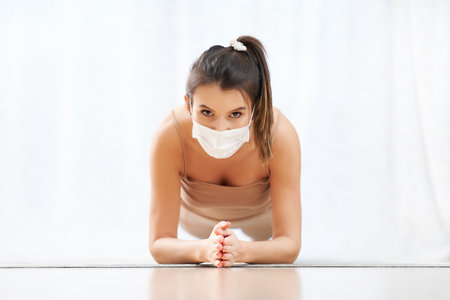 Adult woman practising plank wearing a mask at home