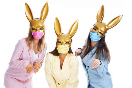 Three women in pastel suits bunny ears and masks posing over white background