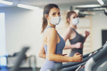 Two girl friends working out on treadmill in masksの写真素材
