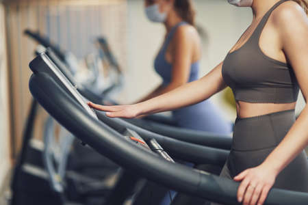 Two girl friends working out on treadmill in masksの写真素材