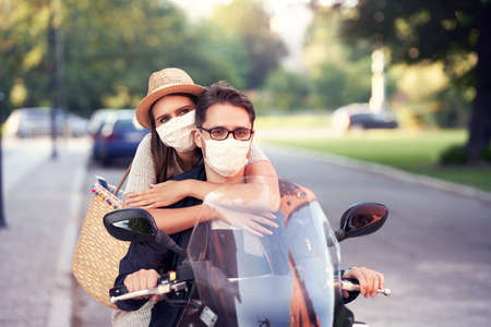 Happy mature couple wearing masks while riding a scooter in the city on a sunny dayの写真素材