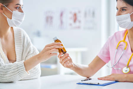 Doctor in mask explaining diagnosis to her female patientの写真素材