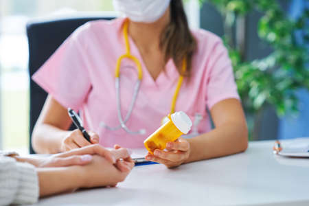 Doctor in mask explaining diagnosis to her female patientの写真素材