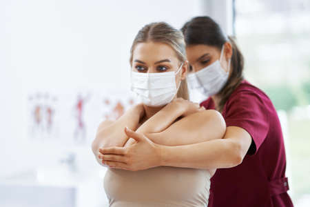 Physiotherapist in mask helping female patientの写真素材