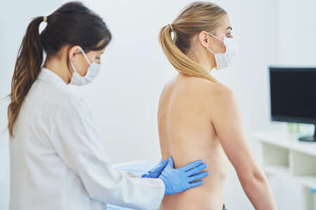 Doctor in mask checking up breast to her patientの写真素材