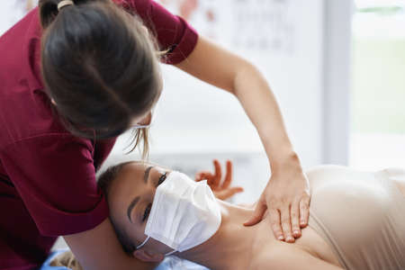 Physiotherapist in mask helping female patientの写真素材