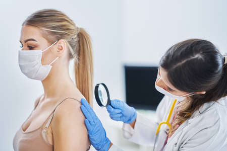Dermatologist in mask checking up on her female patientの写真素材