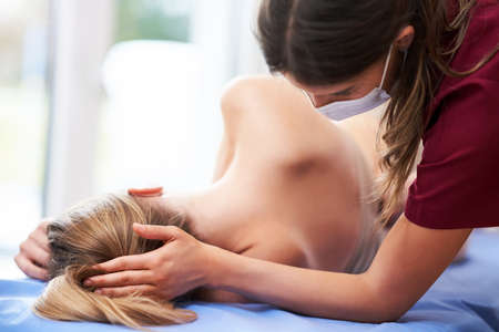 Physiotherapist in mask helping female patientの写真素材