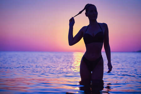 Silhouette of sexy woman posing at sunrise at the beachの写真素材