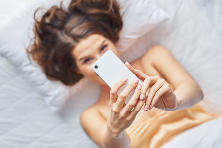 Happyadult woman using smartphone in bedroom in the morningの写真素材