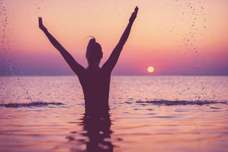 Silhouette of young woman practicing yoga on the beach at sunriseの写真素材