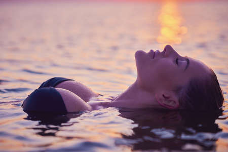 Silhouette of young woman practicing yoga on the beach at sunriseの写真素材