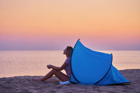 Silhouette of young woman in front of a tent at the beach at sunriseの写真素材