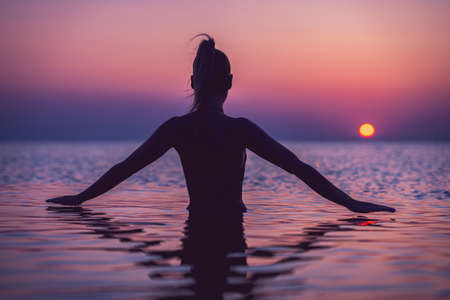 Silhouette of young woman practicing yoga on the beach at sunriseの写真素材