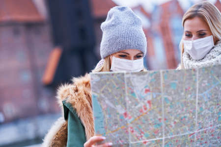 Two women wearing masks and holding map while sightseeing Gdank in Poland