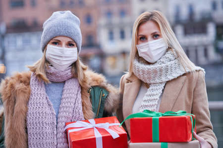 Two women wearing masks and holding Christmas presents in the city