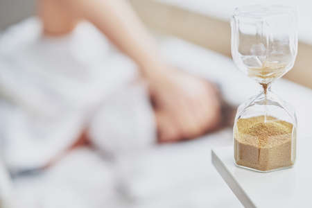 Adult woman in mask feeling sick at home with hourglassの写真素材