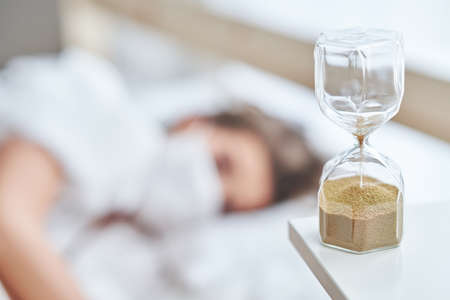 Adult woman in mask feeling sick at home with hourglassの写真素材