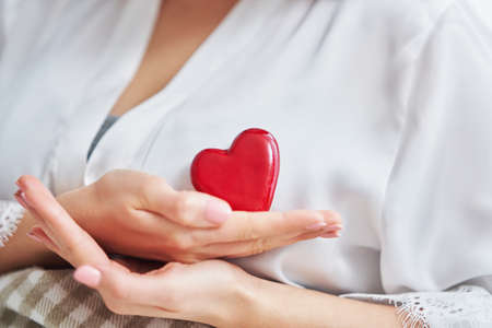 Adult woman in mask showing heart shape at home Covid-19 conceptの写真素材
