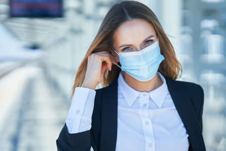 Elegant woman in mask walking with bag and suitcase in the railway stationの写真素材
