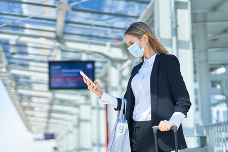 Elegant woman in mask walking with bag and suitcase in the railway stationの写真素材