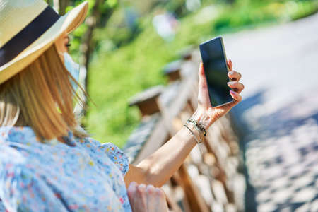 Woman in mask with phone in the park.