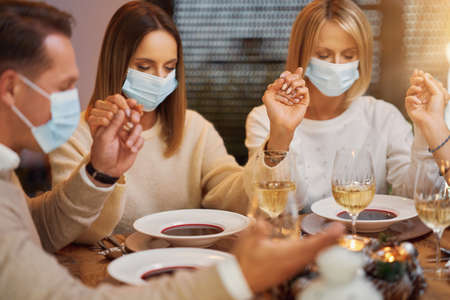 Friends praying before christmas dinner wearing mask.