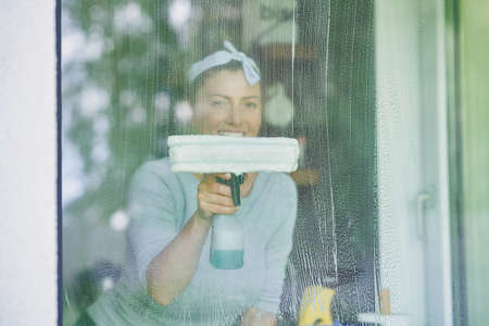 Young woman cleaning window int he kitchen