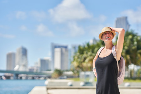 Smiling woman taking selfie with smartphone in sunny urban backdrop, palm trees and cityscape of Miamiの写真素材