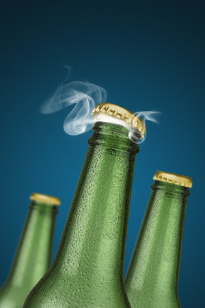 Green cold beer bottles with water drops and golden cap open on blue backgroundの写真素材