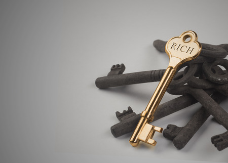 A golden key sitting on top of some rusted ones with the word rich engraved on itの写真素材
