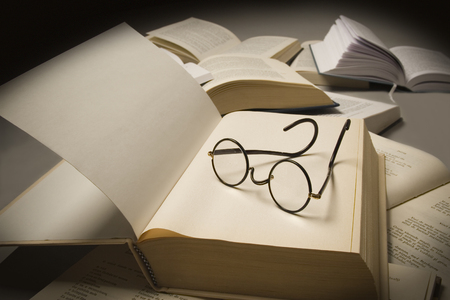 Pair of reading glasses on top of an open book, near other open booksの写真素材