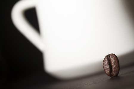 Macro shot of a coffee bean with a white coffee cup silhouette in the backgroundの写真素材