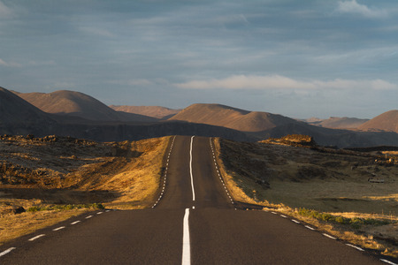 Horizontal photo at sunset of a straight asphalt road going into the mountains with clouds above in Reykjanes peninsula, Icelandの写真素材