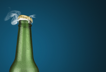 Horizontal photo of a green cold beer bottle with water drops and golden cap open on blue backgroundの写真素材