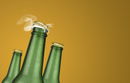 Horizontal photo of three green cold beer bottles with water drops and golden cap open on yellow backgroundの写真素材