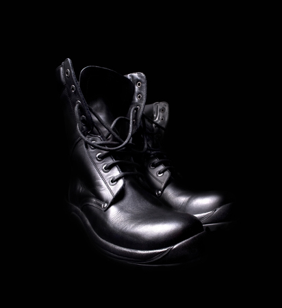 side view of a pair of shiny black leather boots with untied shoe laces on black backgroundの写真素材