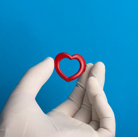 Little red heard held by a hand with a medical white glove on blue background